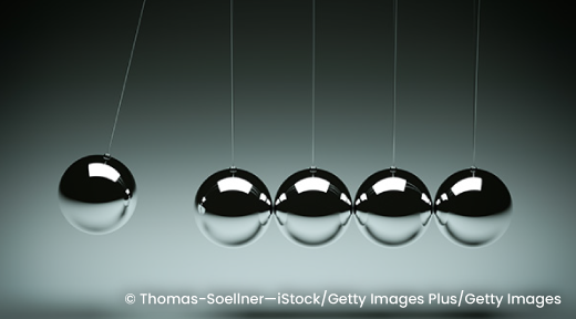 The steel balls of a Newton’s cradle with one ball lifted in anticipation of starting the reaction.