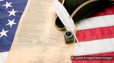 composite image of the United States constitution over an American flag with a feather pen and ink