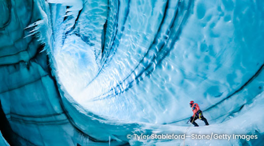 A person standing inside an ice cave formed inside a glacier.